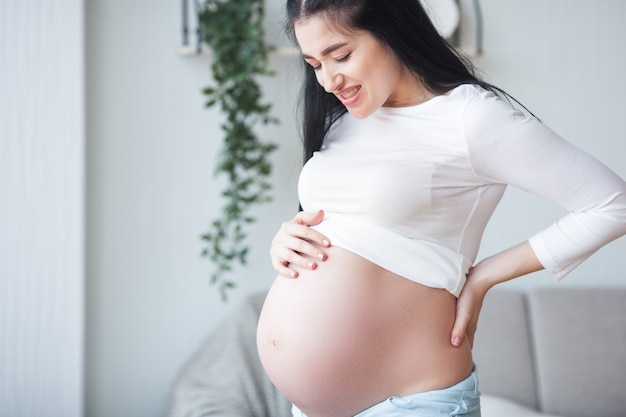 Jonge zwangere vrouw die een rugpijn heeft. Verwacht dat de vrouw zich slecht voelt. Zwangere vrouw die aan pijn lijdt.