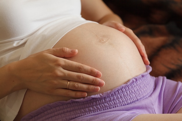 Jonge zwangere vrouw die en wat betreft haar buik, close-up houdt