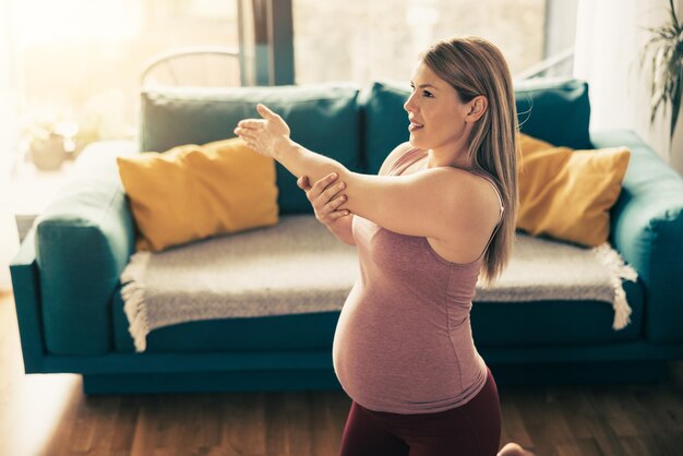 Jonge zwangere vrouw die 's ochtends thuis traint. Ze doet rekoefeningen.