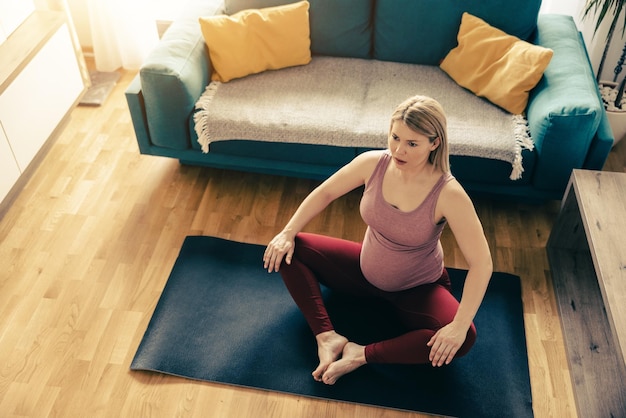 Jonge zwangere vrouw die 's ochtends thuis yoga uitoefent. Ze doet rekoefeningen in haar woonkamer.