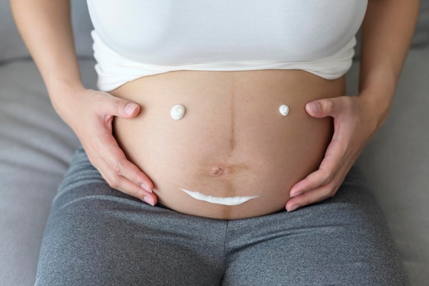 Jonge zwangere vrouw die vochtinbrengende crème aanbrengt op buikgezondheidszorg en zwangerschapszorg