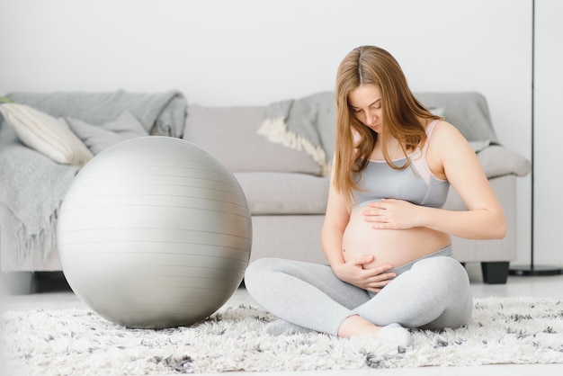 Jonge zwangere vrouw die yoga met fit bal thuis uitoefent. Gezond sportzwangerschapsconcept