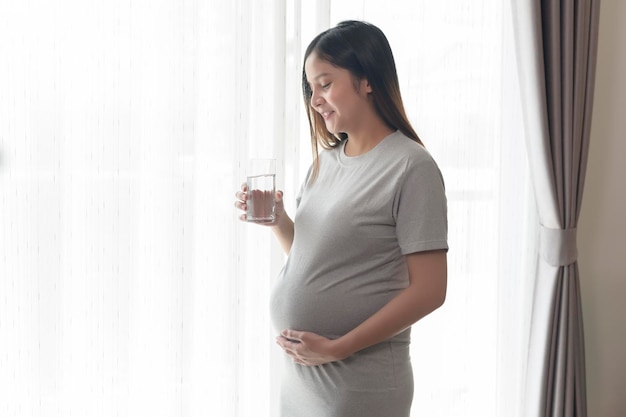 Jonge zwangere vrouw drinkwater thuis gezondheidszorg en zwangerschap zorgconcept