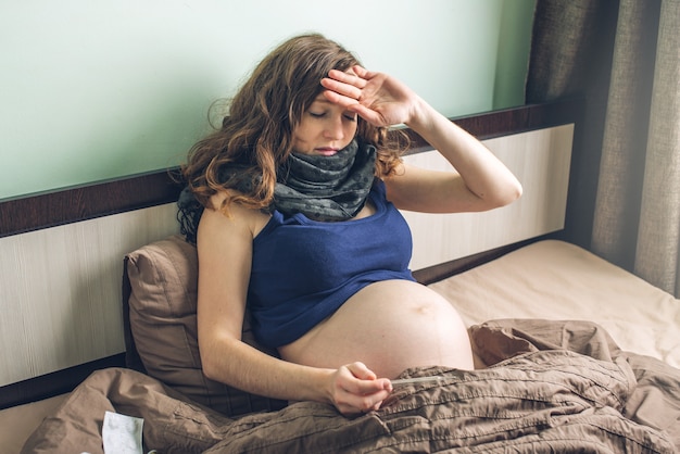 Foto jonge zwangere vrouw in bed met pillen en een thermometer