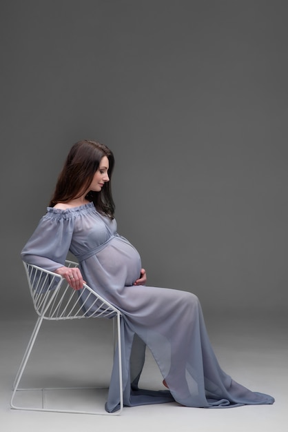 Jonge zwangere vrouw in een jurk zit op een stoel