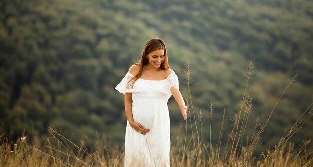 Jonge zwangere vrouw in witte jurk op het zomer-veld