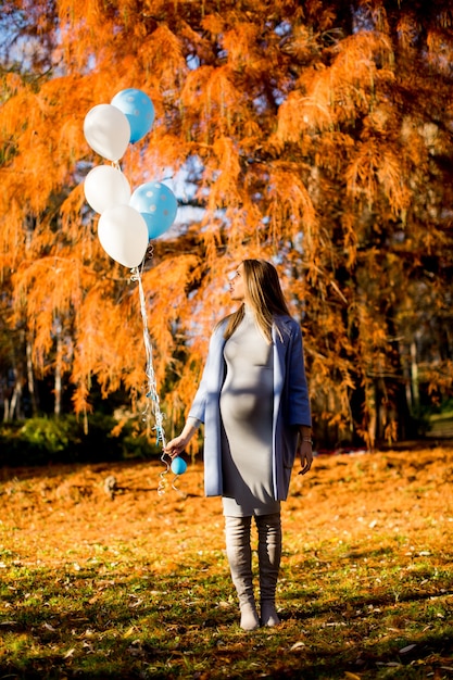 Jonge zwangere vrouw loopt in herfst park met ballonnen in de hand