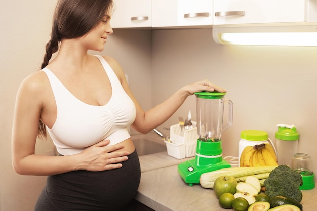 Jonge zwangere vrouw maakt thuis een groene gezonde smoothie