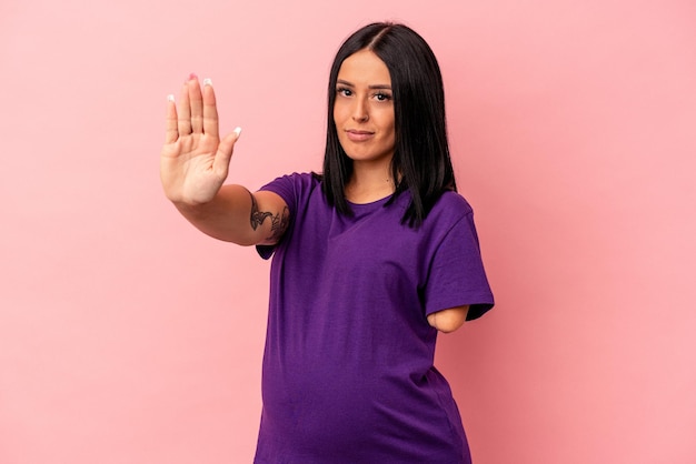 Jonge zwangere vrouw met één arm geïsoleerd op roze achtergrond permanent met uitgestrekte hand weergegeven: stopbord, voorkomen dat u.