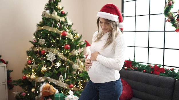 Jonge zwangere vrouw met een kerstmuts die haar buik thuis aanraakt