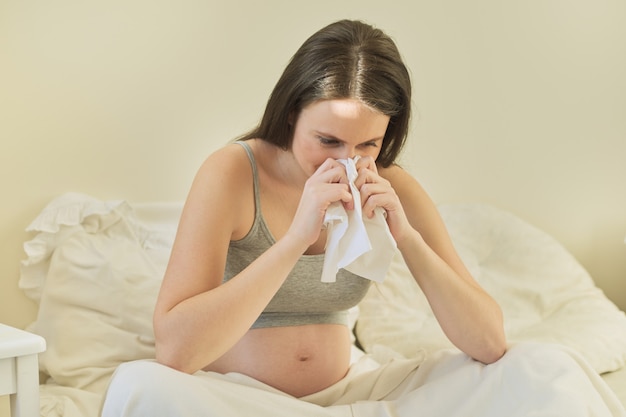 Jonge zwangere vrouw met zakdoekzitting in bed thuis