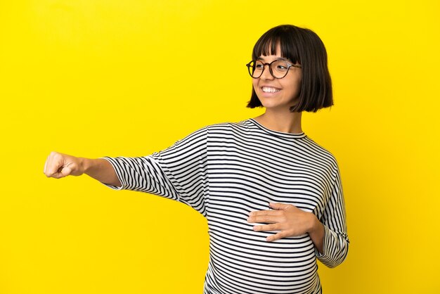 Jonge zwangere vrouw over geïsoleerde gele achtergrond die een duim omhoog gebaar geeft