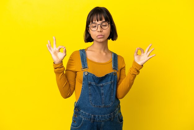 Jonge zwangere vrouw over geïsoleerde gele achtergrond in zen pose