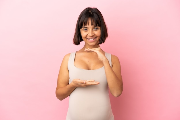 Jonge zwangere vrouw over geïsoleerde roze achtergrond die copyspace denkbeeldig op de palm houdt om een advertentie in te voegen