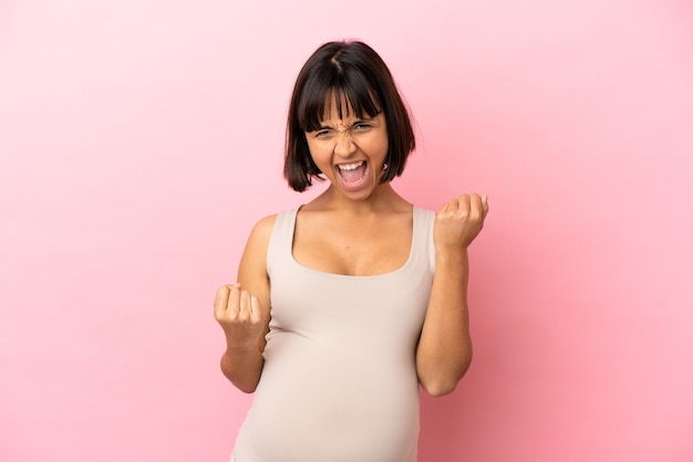 Jonge zwangere vrouw over geïsoleerde roze achtergrond die een overwinning viert