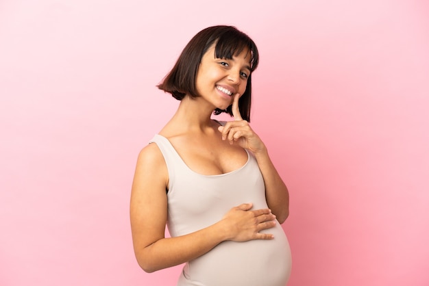 Jonge zwangere vrouw over geïsoleerde roze achtergrond glimlachend met een gelukkige en aangename uitdrukking