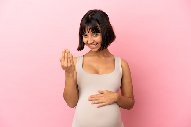 Jonge zwangere vrouw over geïsoleerde roze muur die uitnodigt om met de hand te komen