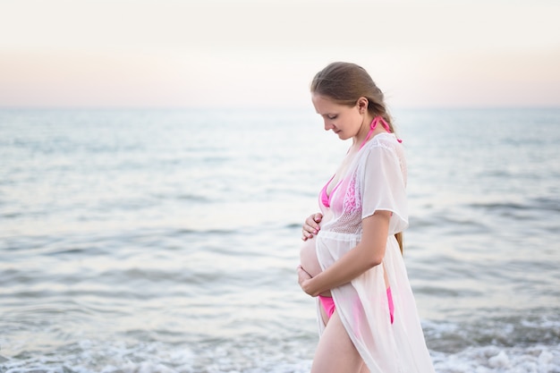 Jonge zwangere vrouw staat aan de kust en knuffelt haar buik. Genieten van het moment