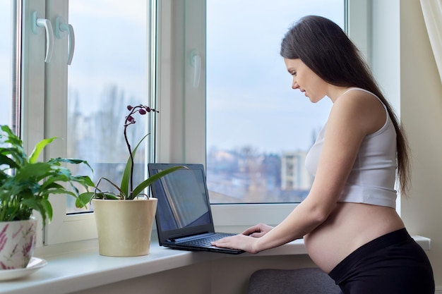 Jonge zwangere vrouw thuis met laptop