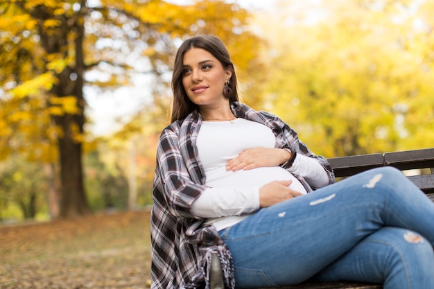 Jonge zwangere vrouw zitten in de herfst park