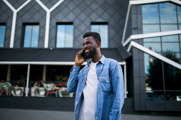 Jonge zwarte Afrikaanse man glimlachend en praten op mobiele telefoon buiten
