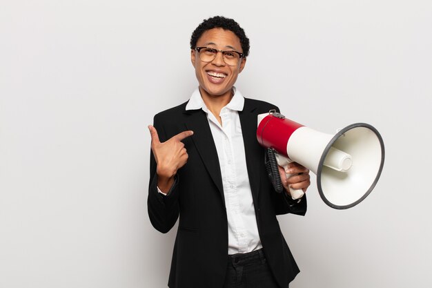 Jonge zwarte afro-vrouw die zich blij, verrast en trots voelt en naar zichzelf wijst met een opgewonden, verbaasde blik