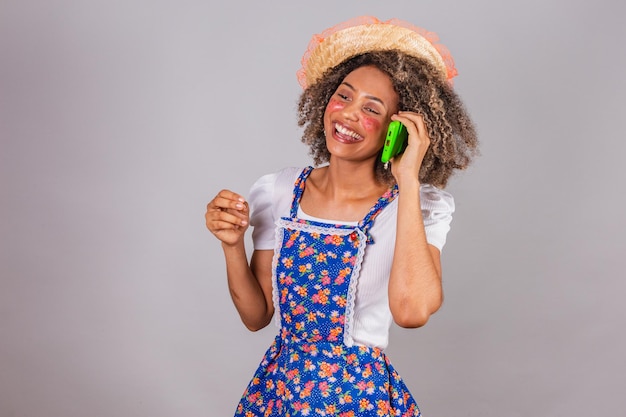 Jonge zwarte Braziliaanse vrouw met landelijke kleding gekleed voor Festa Junina Saint John's festival op spraakoproep met smartphone