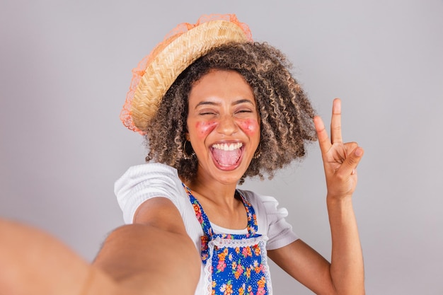 Jonge zwarte Braziliaanse vrouw met landelijke kleding gekleed voor Festa Junina Saint John's festival poseren voor selfie met smartphone