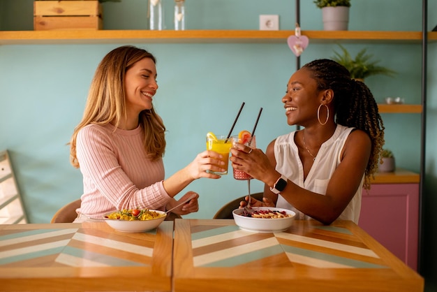 Jonge zwarte en blanke vrouw die plezier heeft met het drinken van verse sappen en een gezond ontbijt in het café