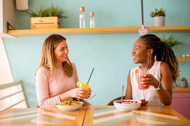 Jonge zwarte en blanke vrouw die plezier heeft met het drinken van verse sappen en een gezond ontbijt in het café