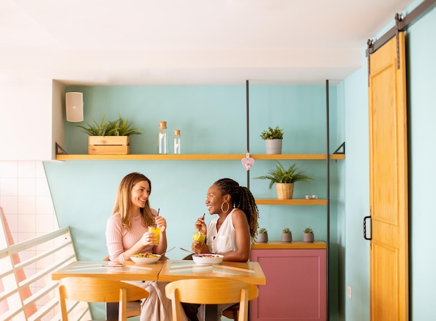 Jonge zwarte en blanke vrouw die plezier heeft met het drinken van verse sappen en een gezond ontbijt in het café