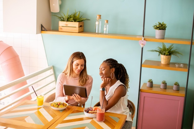 Jonge zwarte en blanke vrouw die plezier heeft met het drinken van verse sappen en een gezond ontbijt in het café