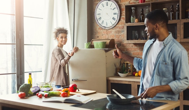 Foto jonge zwarte familie bereidt samen diner in de keuken. man duim opdagen voor vrouw