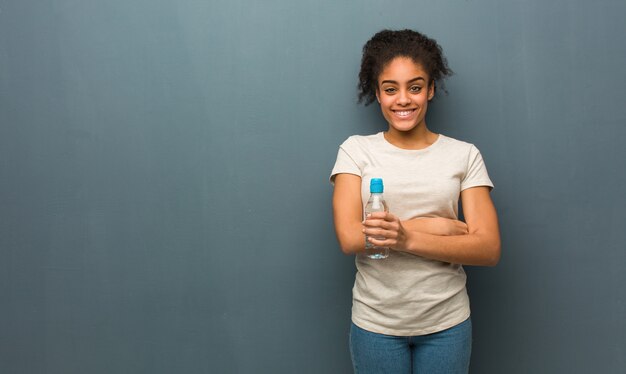 Jonge zwarte kruising armen, glimlachend en ontspannen. ze houdt een fles water vast.
