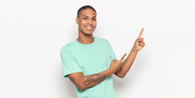 Jonge zwarte man die vrolijk lacht en naar de zijkant en naar boven wijst met beide handen die een object in de kopieerruimte tonen