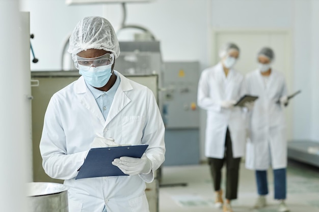 Jonge zwarte man met een masker en een klembord in een fabriekswerkplaats