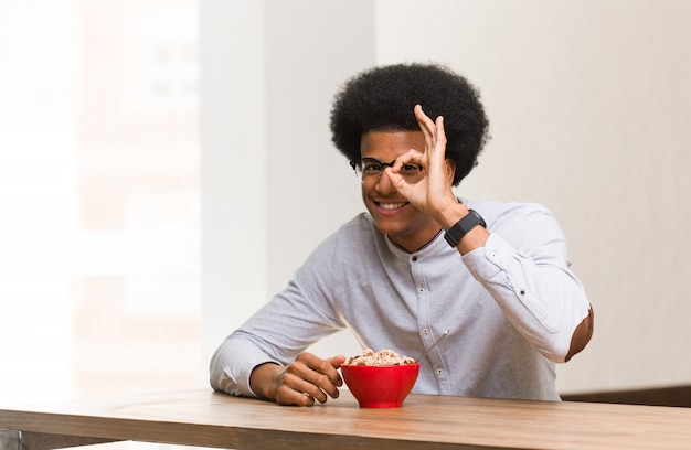 Jonge zwarte man met een ontbijt zeker doen ok gebaar op oog