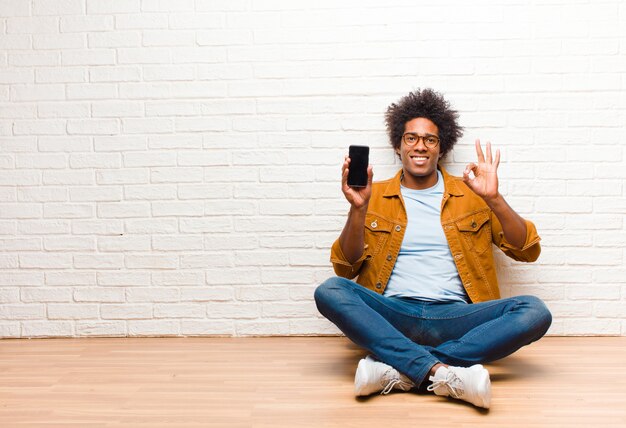 Jonge zwarte man met een slimme telefoon zittend op de vloer