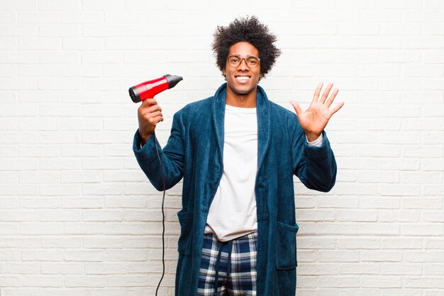 Jonge zwarte man met pyjama's met een föhn tegen baksteen