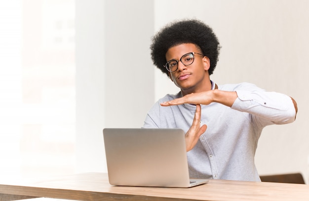 Jonge zwarte man met zijn laptop doet een time-out gebaar