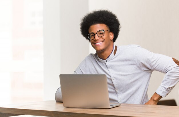 Jonge zwarte man met zijn laptop met handen op de heupen