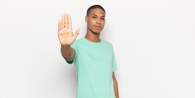 Jonge zwarte man op zoek ernstig, streng, ontevreden en boos met open palm stop gebaar maken