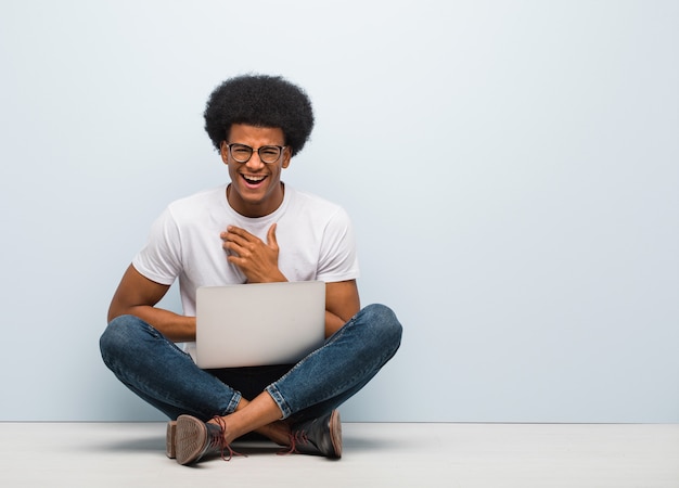 Jonge zwarte man zittend op de vloer met een laptop lachen en plezier maken