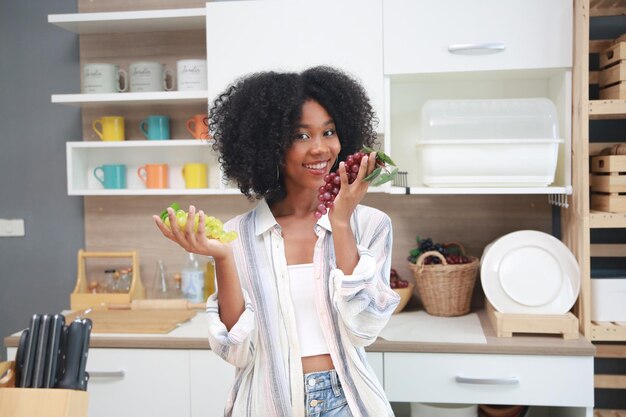 Jonge zwarte meid met afro-haarvrouw die fruit bereidt en eet voordat ze een smoothie maakt