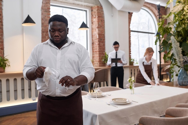 Jonge zwarte restaurantwerker die wijnglazen schoonmaakt
