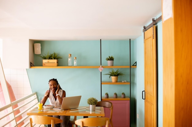 Jonge zwarte vrouw die een gezond ontbijt heeft terwijl ze aan een laptop werkt in het café