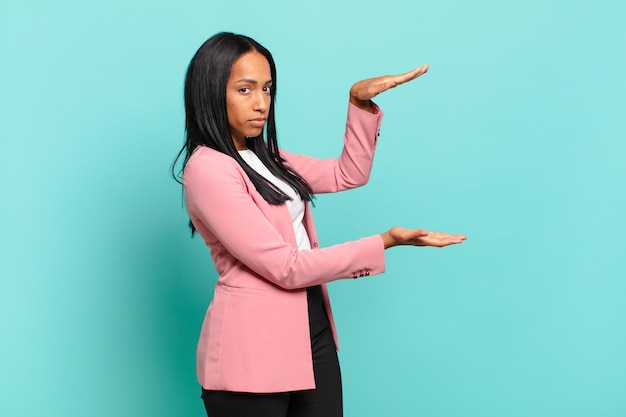 Jonge zwarte vrouw die een object vasthoudt met beide handen op de zijkopieerruimte, een object toont, aanbiedt of adverteert. bedrijfsconcept