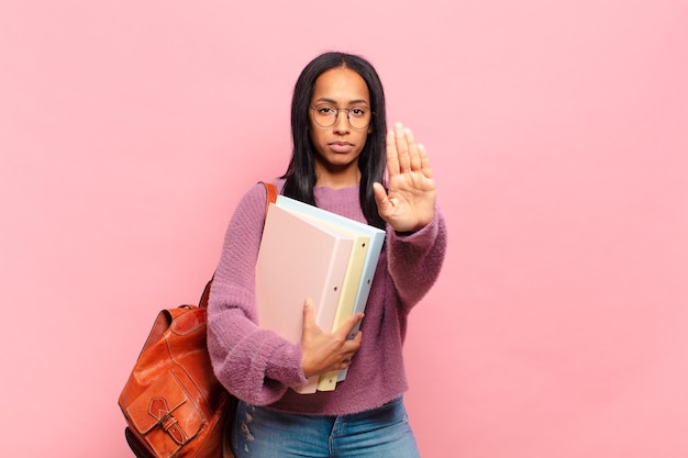 Jonge zwarte vrouw die er serieus, streng, ontevreden en boos uitziet met een open palm die een stopgebaar maakt. studentenconcept