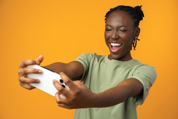 Jonge zwarte vrouw die smartphone gebruikt tegen gele studioachtergrond