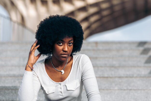 Jonge zwarte vrouw die zich voordeed op een trap in de straat en met haar hand haar afro-haar streelde